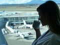 CLOSE UP: Happy young woman drinks her morning tea while watching busy airport. Royalty Free Stock Photo