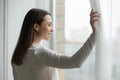 Close up happy young woman opening curtains, looking out window Royalty Free Stock Photo