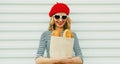 Close up of happy young woman wearing a french red beret looking on a paper bag with long white bread baguette over a white