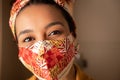 Black woman with protective mask looking at camera. At apartment door entrance. Individuality, style, identity,