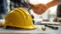 Close-Up of Hard Hat on Engineer's Desk with Blueprints and Tools, Handshake in Background Royalty Free Stock Photo
