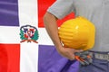 Hand of worker and yellow hard-hat on background flag of Dominican Republic Royalty Free Stock Photo