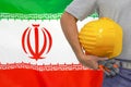 Hand of worker and yellow hard-hat on background flag of Iran Royalty Free Stock Photo