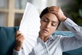 Overheated young indian woman cooling herself with paper fan.