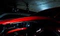 Close up headlight of shiny red luxury SUV compact car parked in shopping mall underground parking lot. Elegant electric car