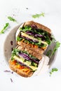 Close up healthy sandwiches with arugula, carrot, cheese, red cabbage, wrapped in craft organic paper on a marbre plate