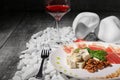 Close-up of healthy snacks on a wooden background. Wineglass, fork and plate of ham, spinach and cheese on white rocks. Royalty Free Stock Photo