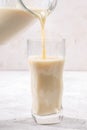 Close-up oat milk is pouring from glass decanter into figured glass