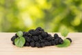 Close-up heap of ripe black mulberries with green leaves on table.
