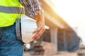 Close-up helmet of Construction worker or civil engineer holding safety white helmet and construction drawing against the Royalty Free Stock Photo