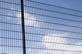 Close-up of high abstract geometrical protective dark metal fence of soccer or football field playground on clear blue sky with br