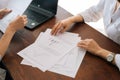 Close-up high-angle view of hands unrecognizable two young business women sitting at desk with laptop and paper