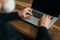 Close-up high-angle view of unrecognizable bearded mature adult male typing on laptop keyboard sitting at table at home