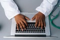 Close-up high-angle view of unrecognizable black practitioner male doctor in white uniform working typing on laptop Royalty Free Stock Photo