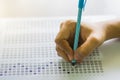 Close up of high school or university student holding a pen writing on answer sheet paper in examination room. College students an