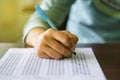 Close up of high school or university student holding a pen writing on answer sheet paper in examination room. College students an