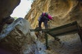 close up of hiker with backpack climbing a stone wall stepping on some green steps to climb the vertical gap of a mountain to get Royalty Free Stock Photo