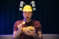 Close up of the hipster man with beer helmet on the head eating chips while watching TV. At home. Indoor Royalty Free Stock Photo