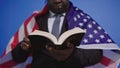 Close up, holy bible in the hands of black african american man in elegant suit with USA flag over the shoulders Royalty Free Stock Photo