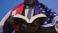 Close up, holy bible in the hands of black african american man in elegant suit with USA flag over the shoulders Royalty Free Stock Photo