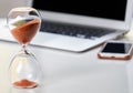 Close up of home office desktop, focus on sandglass, laptop in the background.