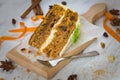 Close up of a homemade carrot cake with raisins, walnuts and cinnamon over white wooden background. Cream cheese frosting.