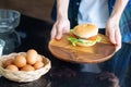 Close-up of a homemade hamburger on a wooden dish, holding by a young man in the kitchen. Junk-food. Unhealthy foods concept Royalty Free Stock Photo