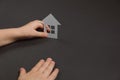 Close up horizontal image of child`s hands holding white paper house on gray background. Family home and real estate concept. Royalty Free Stock Photo