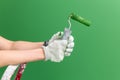 Close up horizontal image of hands in working gloves holding middle-sized roller with green paint in front of green wall Royalty Free Stock Photo