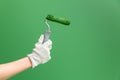 Close up horizontal image of hands in working gloves holding middle-sized roller with green paint in front of green wall Royalty Free Stock Photo