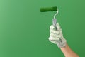 Close up horizontal image of hands in working gloves holding middle-sized roller with green paint in front of green wall Royalty Free Stock Photo