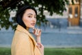 Close up horizontal shot of charming elegant Asian brunette lady, wearing yellow blazer, standing outdoors at city Royalty Free Stock Photo