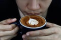 Close up of hot cappuccino coffee in the cafe, Heart shape cream coffee in blue cup. Hands women holding hot coffee in cup Asian Royalty Free Stock Photo