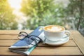 Close up of hot cup of coffee latte with milk heart shape art with newspaper and reading glasses on wooden table Royalty Free Stock Photo