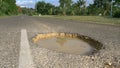 CLOSE UP: Tropical sun shines on large pothole in the middle of decaying road.