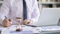 Close Up of Hourglass on Desk and Businessman working on Laptop Royalty Free Stock Photo