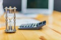 Close-up of hourglass in front of businessperson`s hand calculating invoice using calculator. Royalty Free Stock Photo