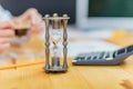 Close-up of hourglass in front of businessperson`s hand calculating invoice using calculator. Royalty Free Stock Photo