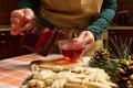 Close-up housewife pouring hibiscus tea from a teapot into a glass cup, standing by a table with gingerbread cookies