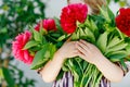 Close-up of huge bouquet of blossoming red and pink peony flowers holding in hands of little toddler girl. Close up of