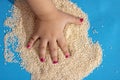 Close-up of human fingers touched handful of white sesame seeds in hand on blue background, kids hands