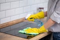 Close up of human hand with protective gloves cleaning induction hob with rag and holding spray bottle Royalty Free Stock Photo