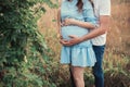 Close up of human hands holding pregnant belly, closeup happy family awaiting baby, standing on green grass, body part, young fami