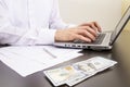 close-up of human hands typing on a computer keyboard. in the foreground are dollar bills Royalty Free Stock Photo