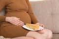 Close up of hungry pregnant woman is eating a piece of tasty cake relaxing on the sofa at home. Sweet cravings during pregnancy Royalty Free Stock Photo