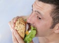 Close-up. A hungry young man eats a big hamburger sandwich with beef, tomatoes, onions, sauce, cheese, lettuce and a sesame bun Royalty Free Stock Photo