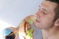 Close-up. A hungry young man eats a big hamburger sandwich with beef, tomatoes, onions, sauce, cheese, lettuce and a sesame bun Royalty Free Stock Photo