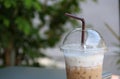 Close up ice coffee in the plastic cup with brown straw and out focus notebook.