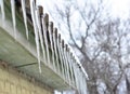 A close-up of the icicles hanging of asbestos roof without a roof gutter. Ice dams on the roof