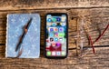 Close-up icons of mobile social media apps on a dark screen of a phone on a wooden background near a pair of glasses and a blue